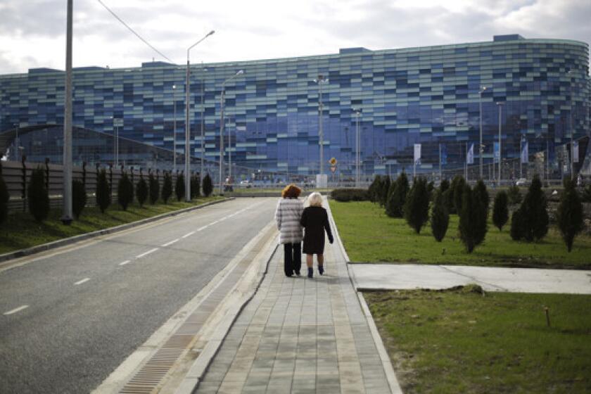 Local residents walk down a street separated by a security perimeter in front of the Iceberg Skating Palace in Sochi, Russia, before the start of the Winter Olympic Games.