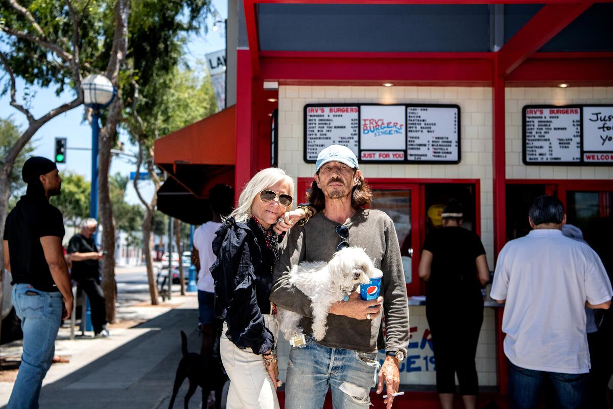 A woman and a man stand in front of the counter of the new Irv's Burgers, holding their little white dog.