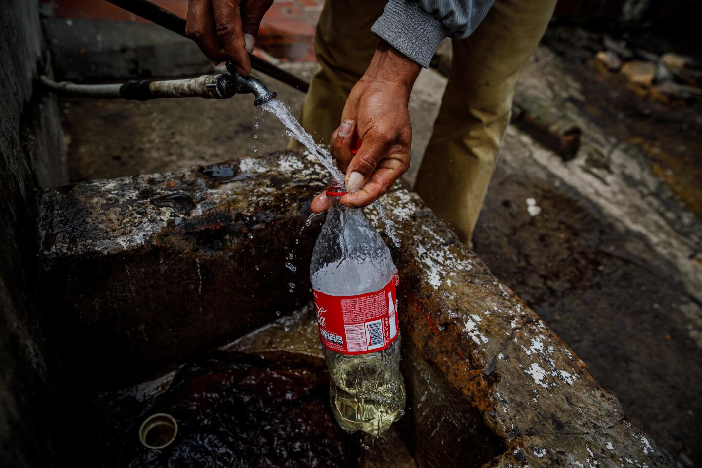 Migrants refill their bottles with discolored water from a tap outside a home.