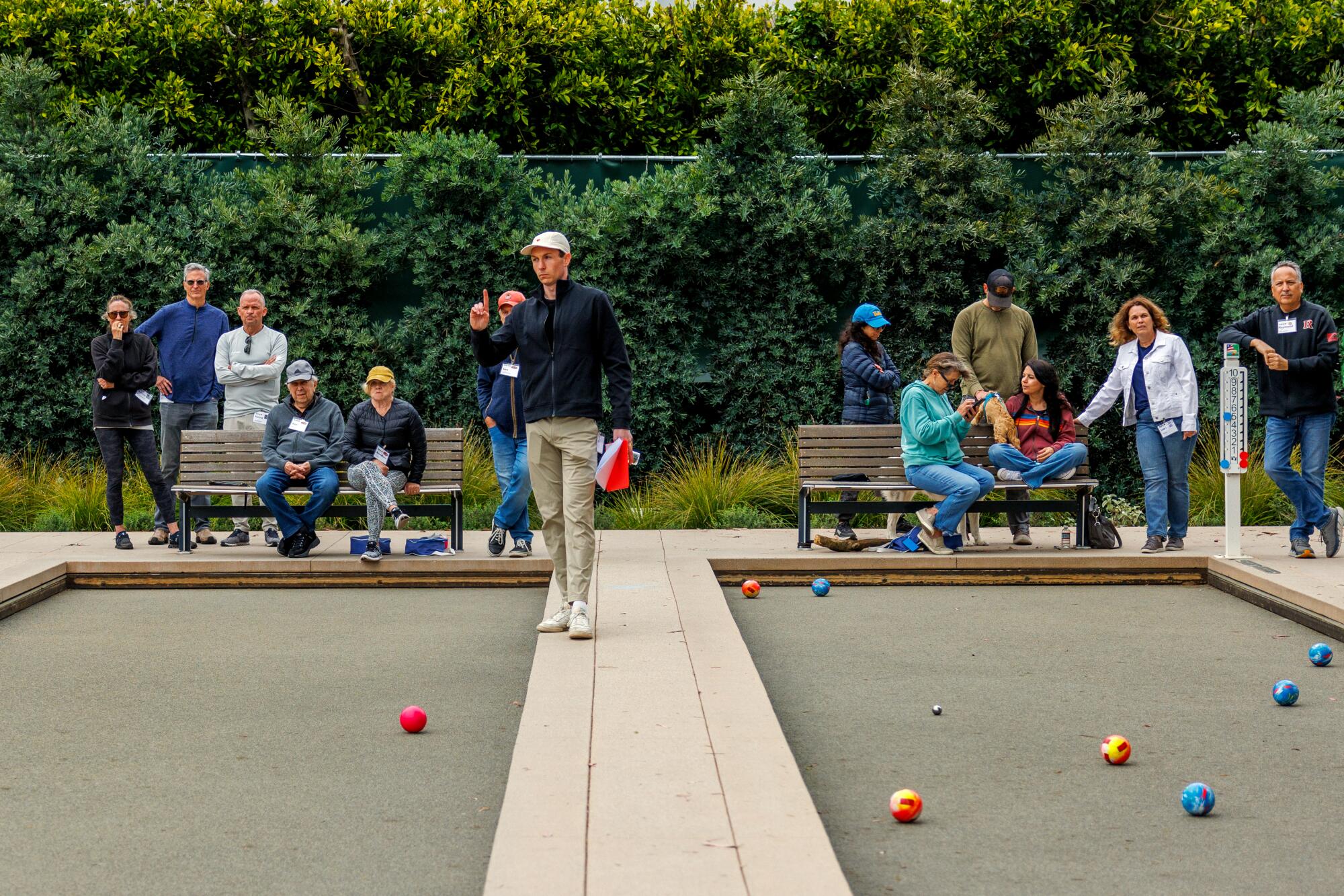 A man walking between bocce courts, counting scores while a crowd watches.
