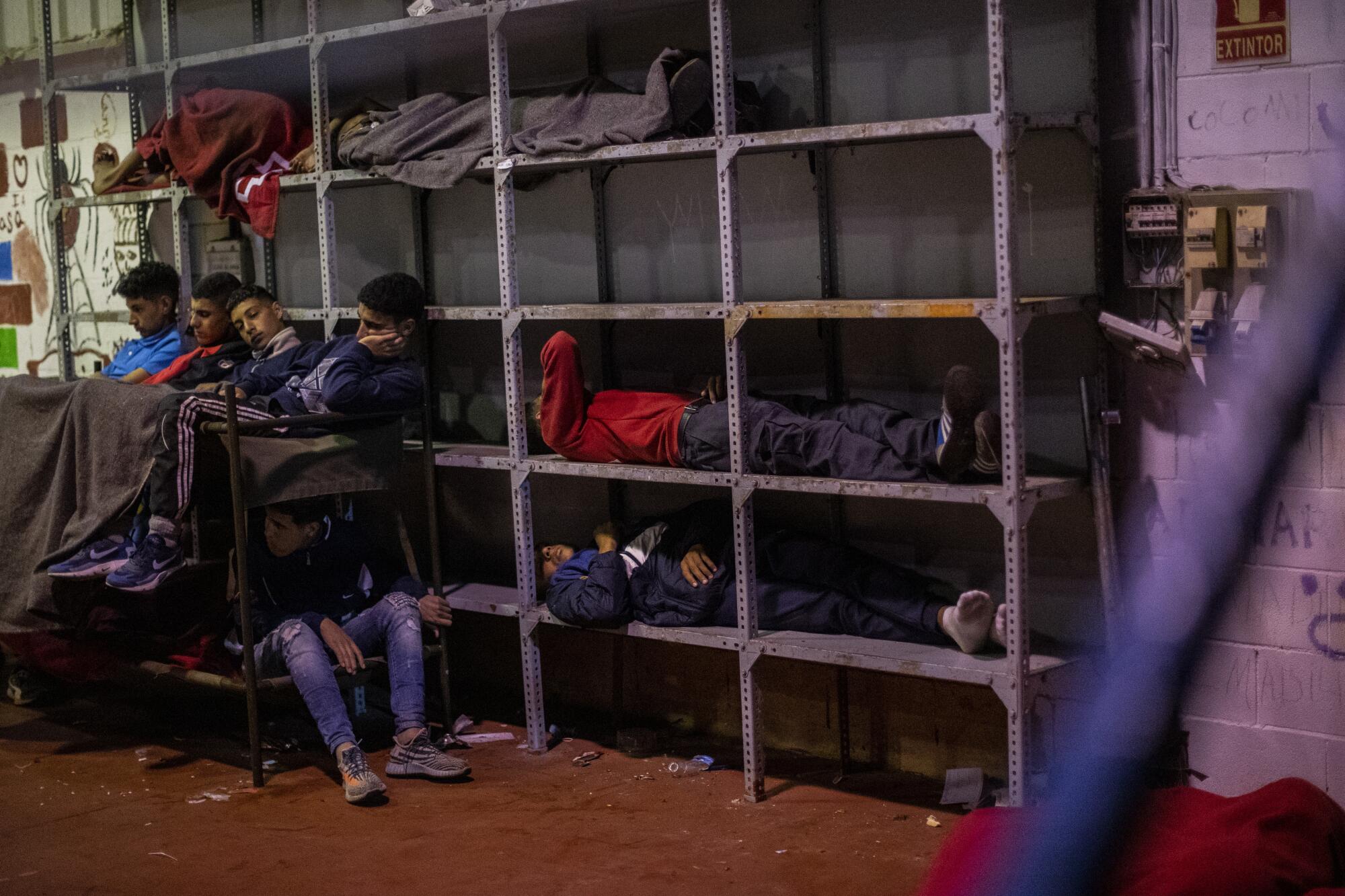 Children and teenage boys huddle together and sleep on cots and metal shelves