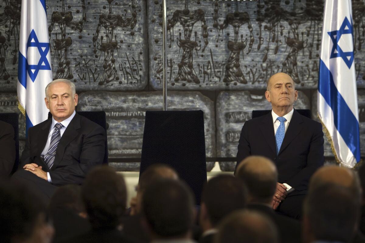 Israeli Prime Minister Benjamin Netanyahu and former Prime Minister Ehud Olmert sit near each other with flags behind them.