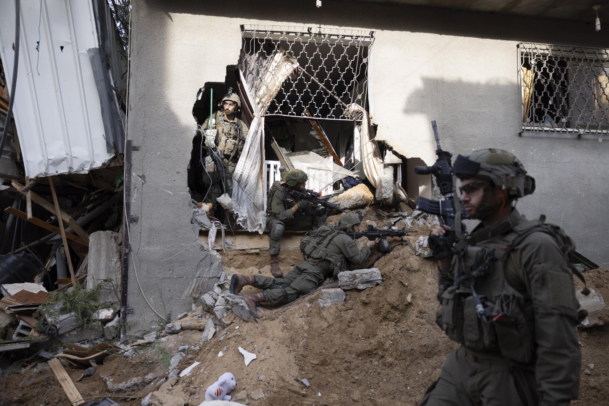 Soldiers take position in a wrecked building, with a large hole punched into a wall