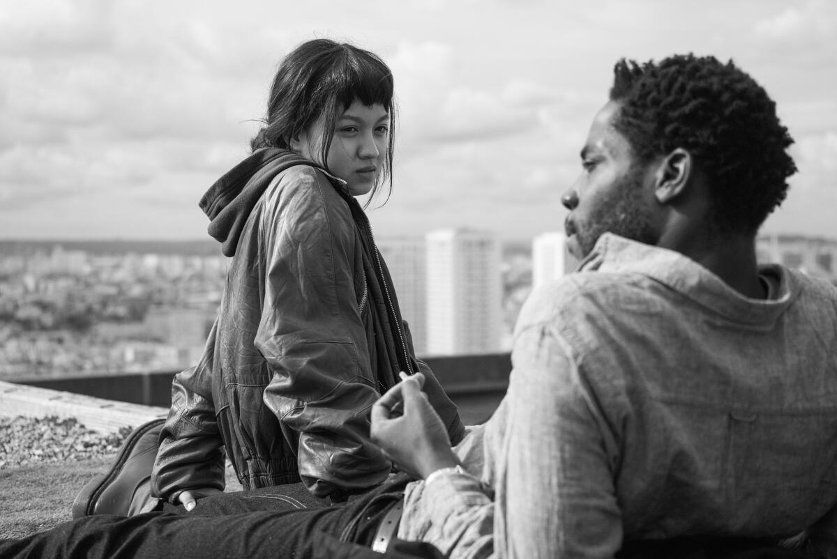 A young woman and man sit on a rooftop in the movie "Paris, 13th District."