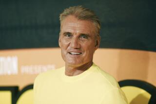 Dolph Lundgren in a yellow shirt smiling and looking over his left shoulder
