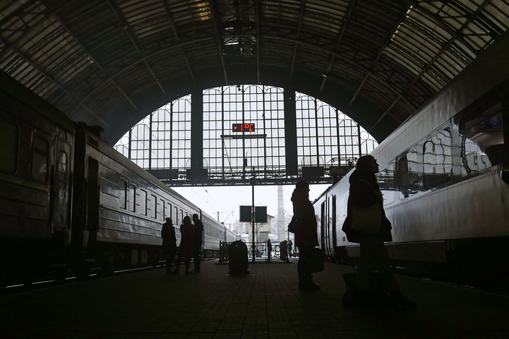 People wait for a train to depart and arrive at a darkened station.