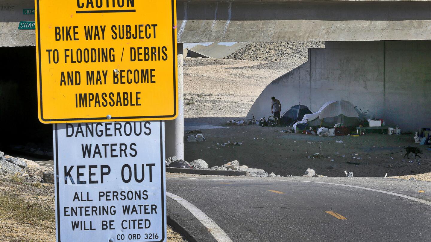 Warning signs are posted in the Santa Ana River channel under the Chapman Avenue overpass in Orange; dozens of homeless camp in the area.