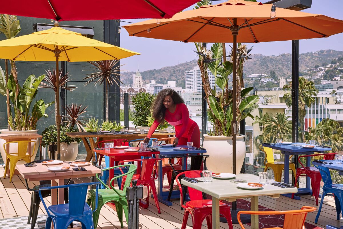 colorful tables, chairs and umbrellas on a rooftop with the Hollywood Hills visible in the distance