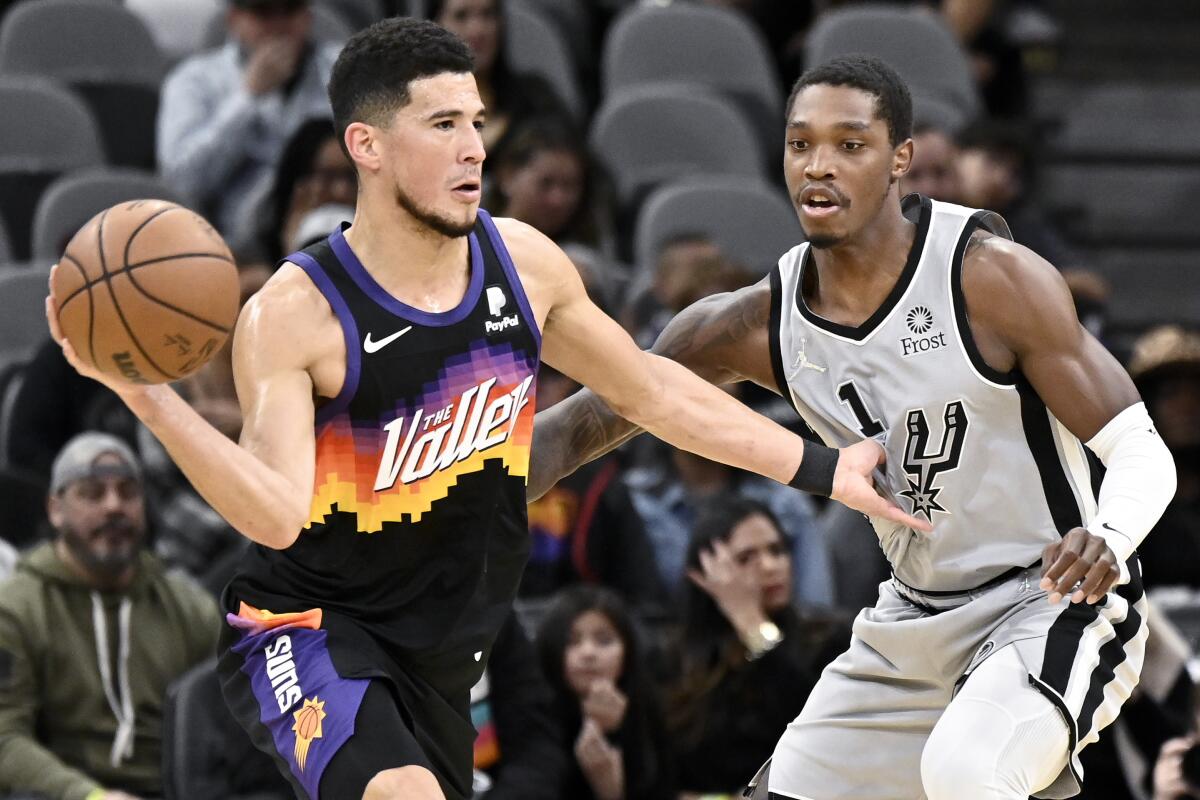 Phoenix Suns' Devin Booker, left, looks to pass the ball as he is defended by San Antonio Spurs' Lonnie Walker IV during the first half of an NBA basketball game, Monday, Nov. 22, 2021, in San Antonio. (AP Photo/Darren Abate)