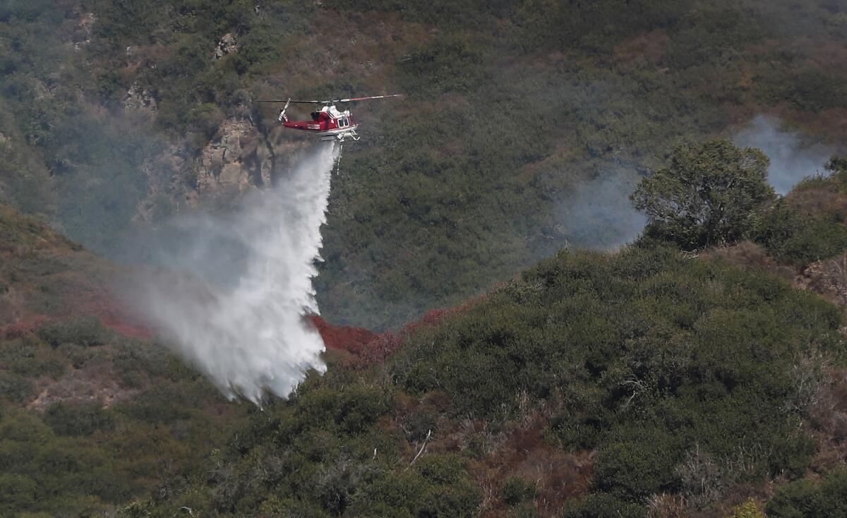 A Cal Fire firefighting plane drops fire retardant on a slope behind in the Arch Beach Heights neighborhood.