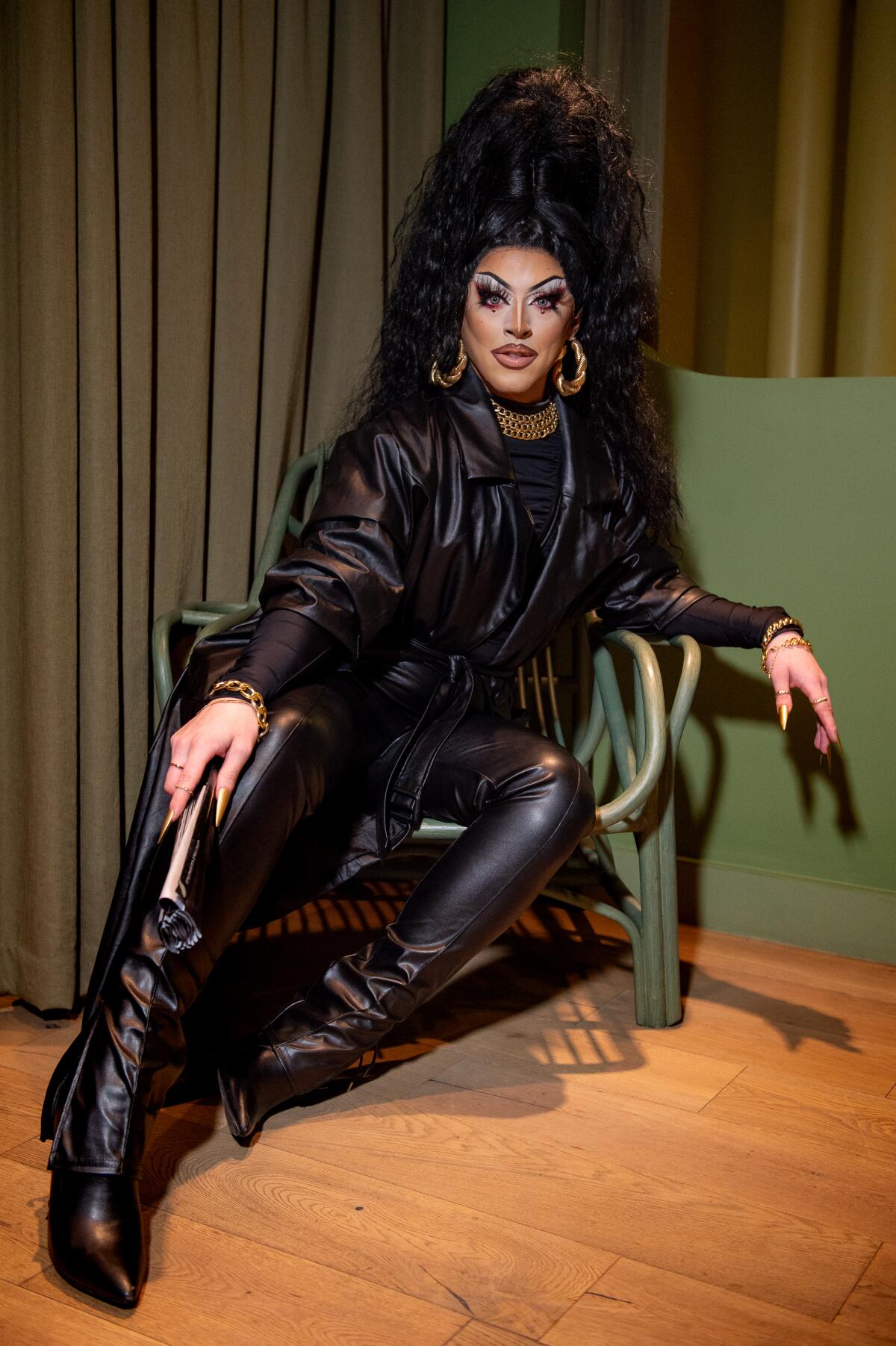 A person with long black hair wearing a black leather coat and black leather boots sitting in a chair