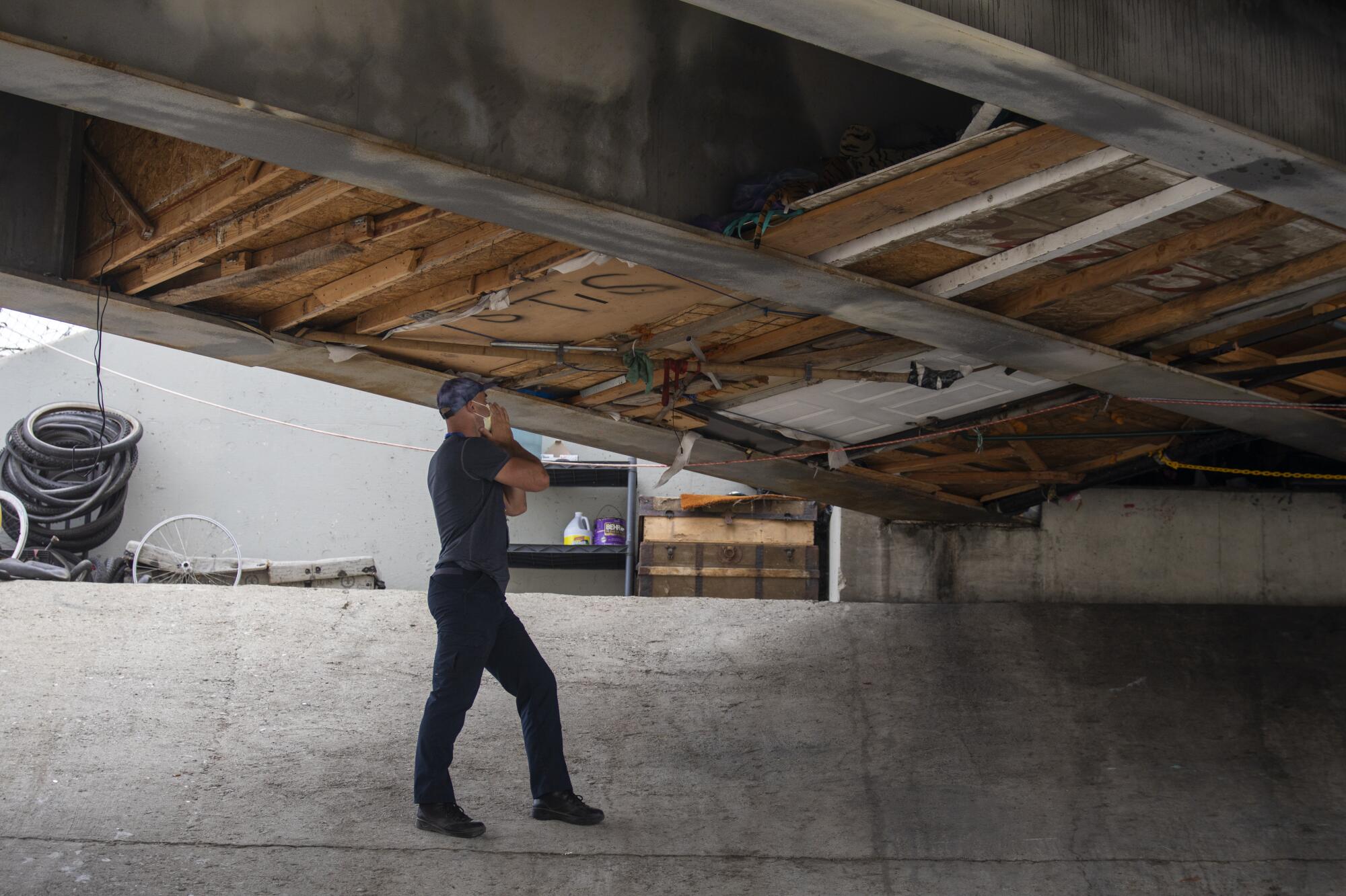 A man stands on sloping concrete, calling to a makeshift shelter perched above the La Canada Verde Creek.