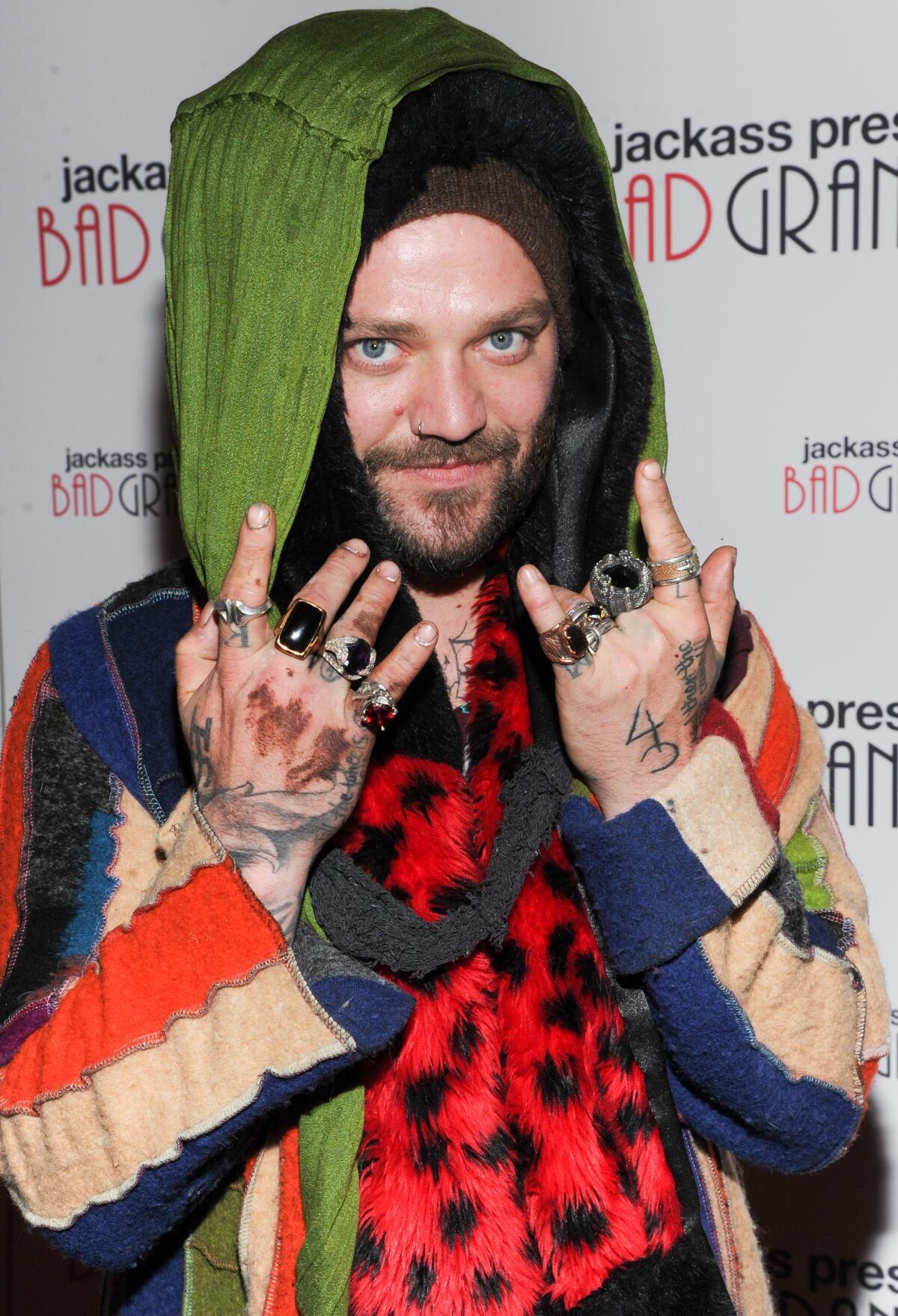 Bam Margera poses in layers of clothing and holds up his hands with many rings.