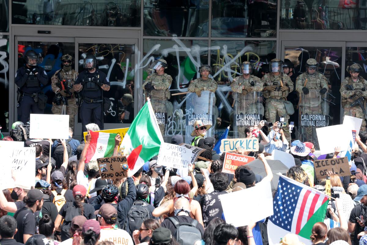 National Guard members stand in front of a building with graffiti on large windows; crowd faces them in foreground