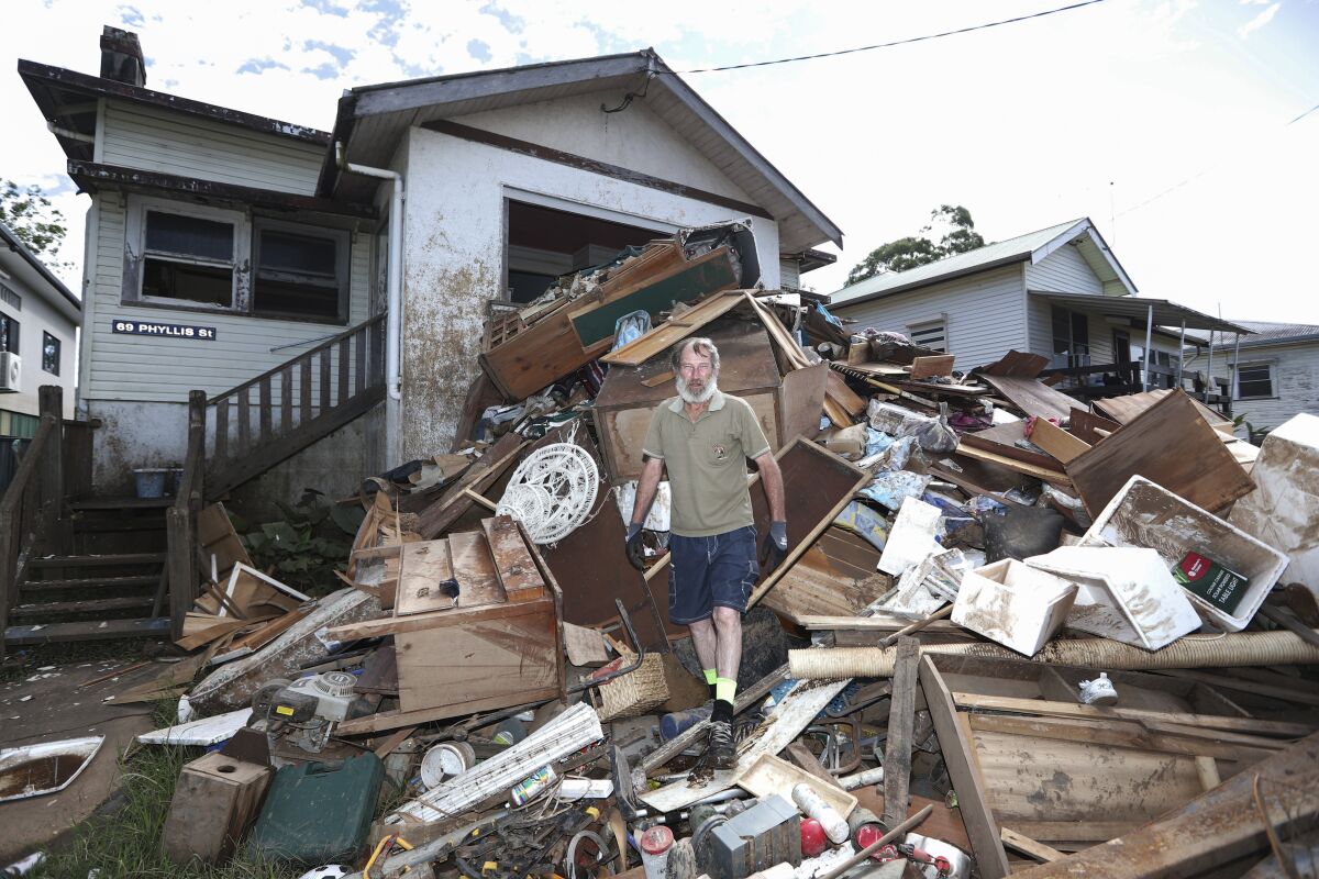 Resident Ken Bridge stands on a pile of his flood-damaged furniture outside his home in Lismore, Australia, Wednesday, March 9, 2022. Australia's Prime Minister Scott Morrison on Wednesday declared a national emergency following floods across large swathes of the east coast that have claimed 21 lives. (Jason O'Brien/AAP Image via AP)