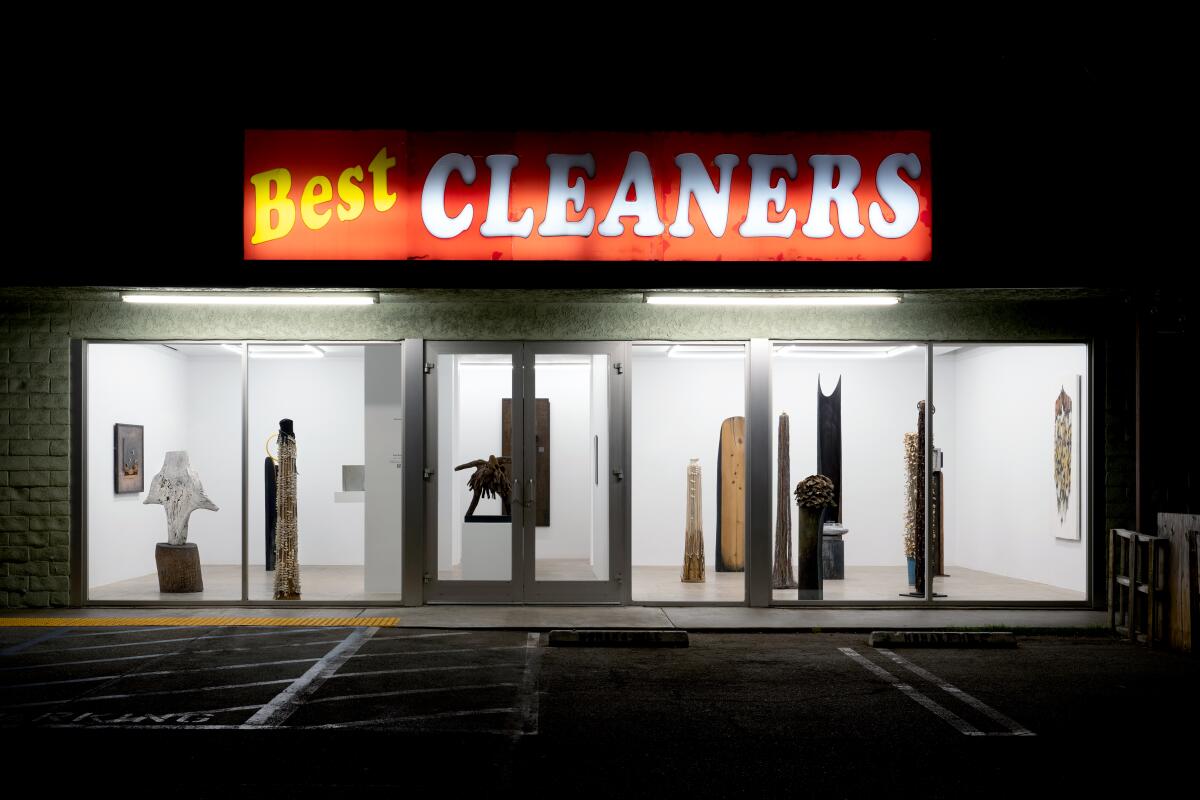 A storefront with a sign that reads "Best Cleaners" is illuminated at night to reveal a series of sculptures.