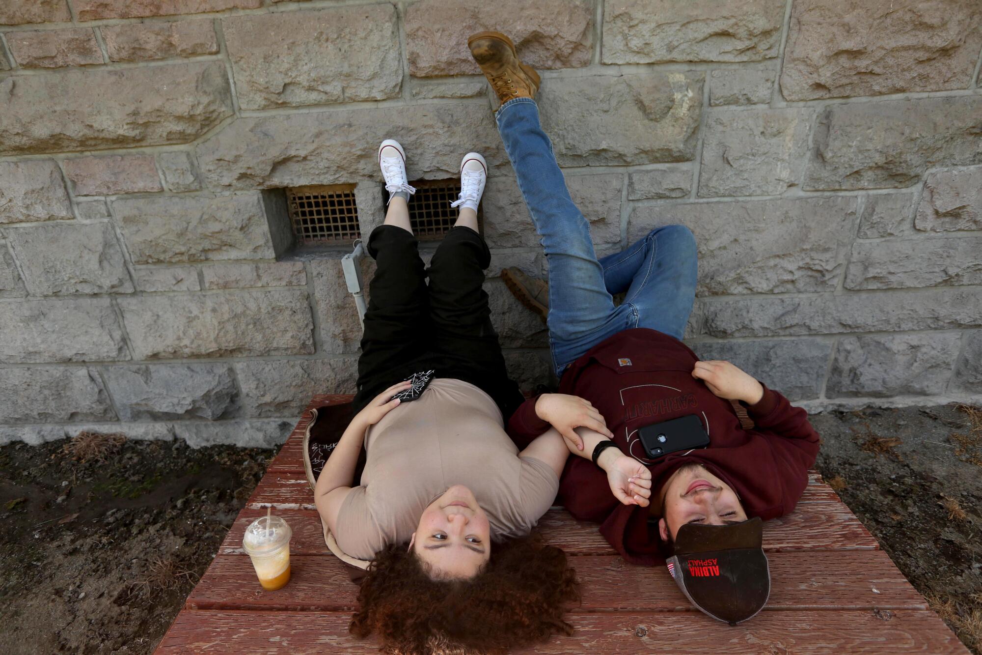 Two students lie on the ground with their feet up against a wall at Modoc High School.