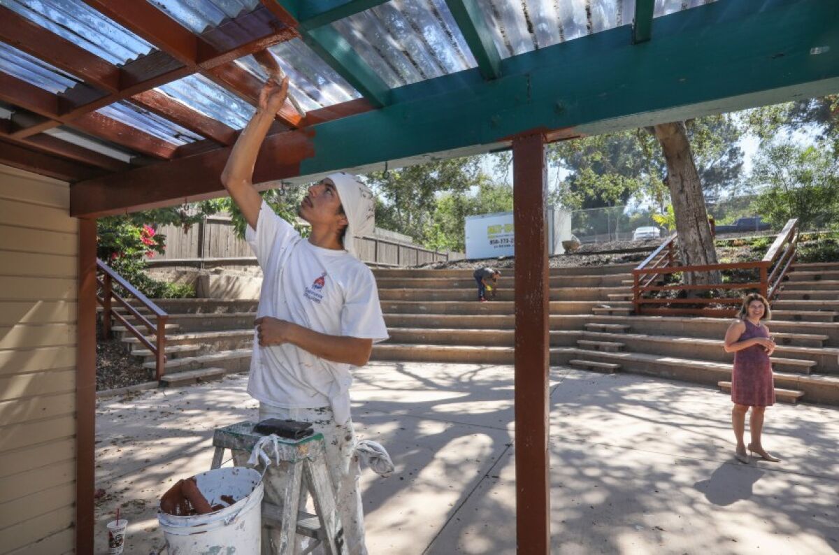 Painter Alder Flores applies finishing touches to an awning at the outdoor amphitheater of the new middle school campus of The Rhoades School in Encinitas. At right is Regina McDuffie, the school’s director.