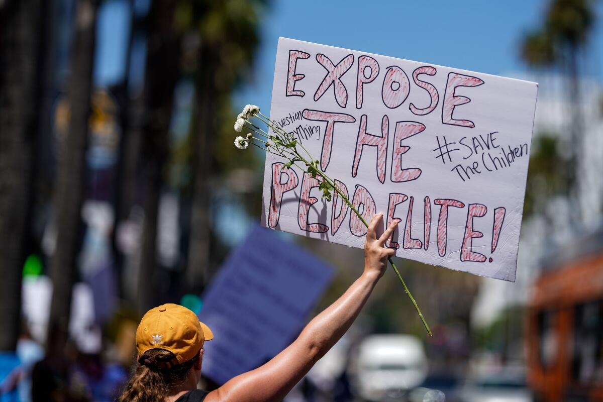 A woman holds a sign reading "Expose the pedo elite" at a protest 