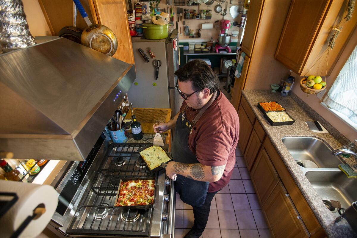 Derek Bracho takes several homemade focaccia-bread pizzas out of the oven at his home in Anaheim.