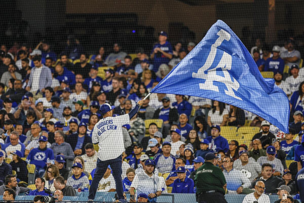 Fans at Dodger Stadium watch a man wave a blue flag with a Dodgers logo.