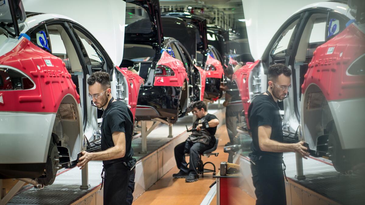 A worker is reflected in a computer screen as he and others assemble cars on the line at Tesla's factory in Fremont.