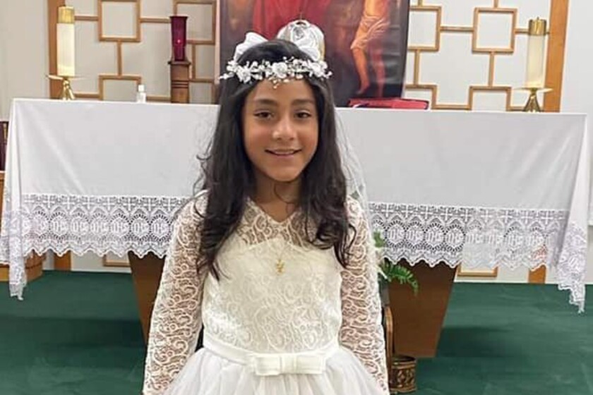 A little girl in a white lace dress and headpiece, standing in front of a church altar