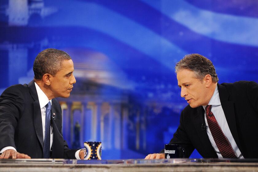 Jon Stewart leans over his desk to talk to President Barack Obama