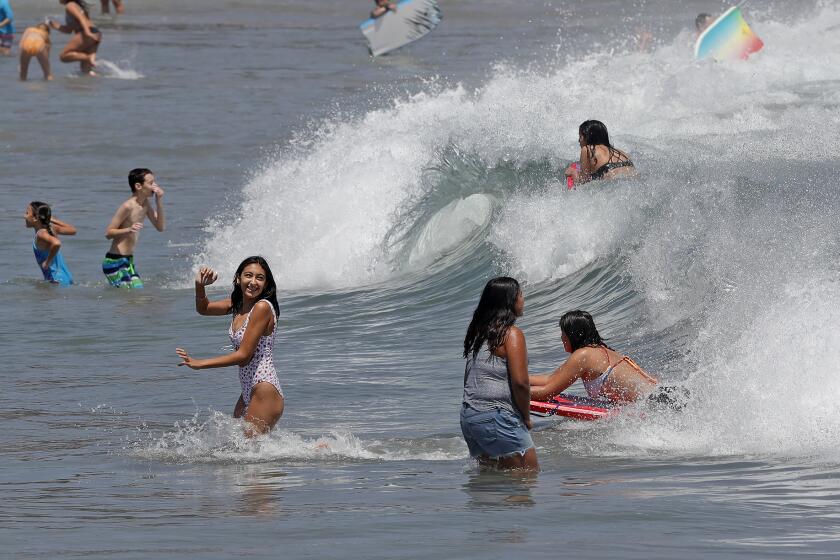 Happy beachgoers jump into the waves at Corona Del Mar State Beach on Tuesday.