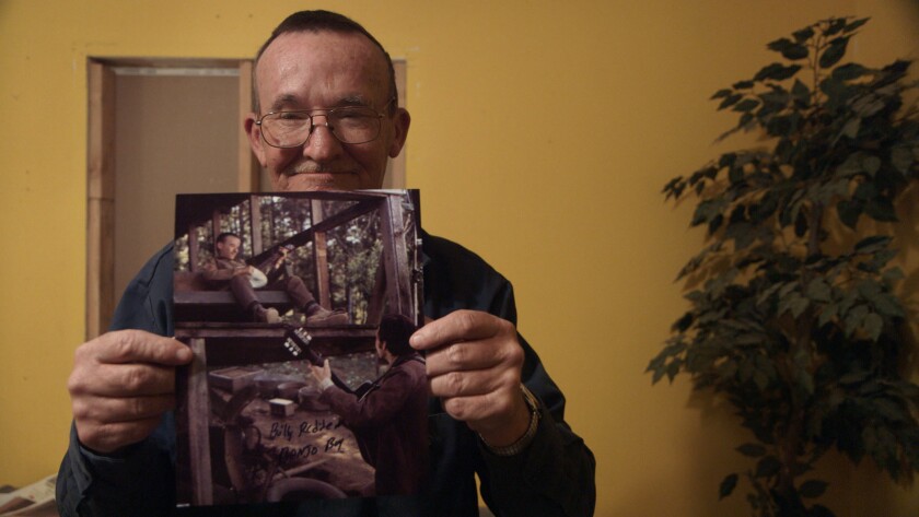 In the documentary "Hillbilly," Billy Redden poses with photos from his acting debut in the 1972 film "Deliverance,"