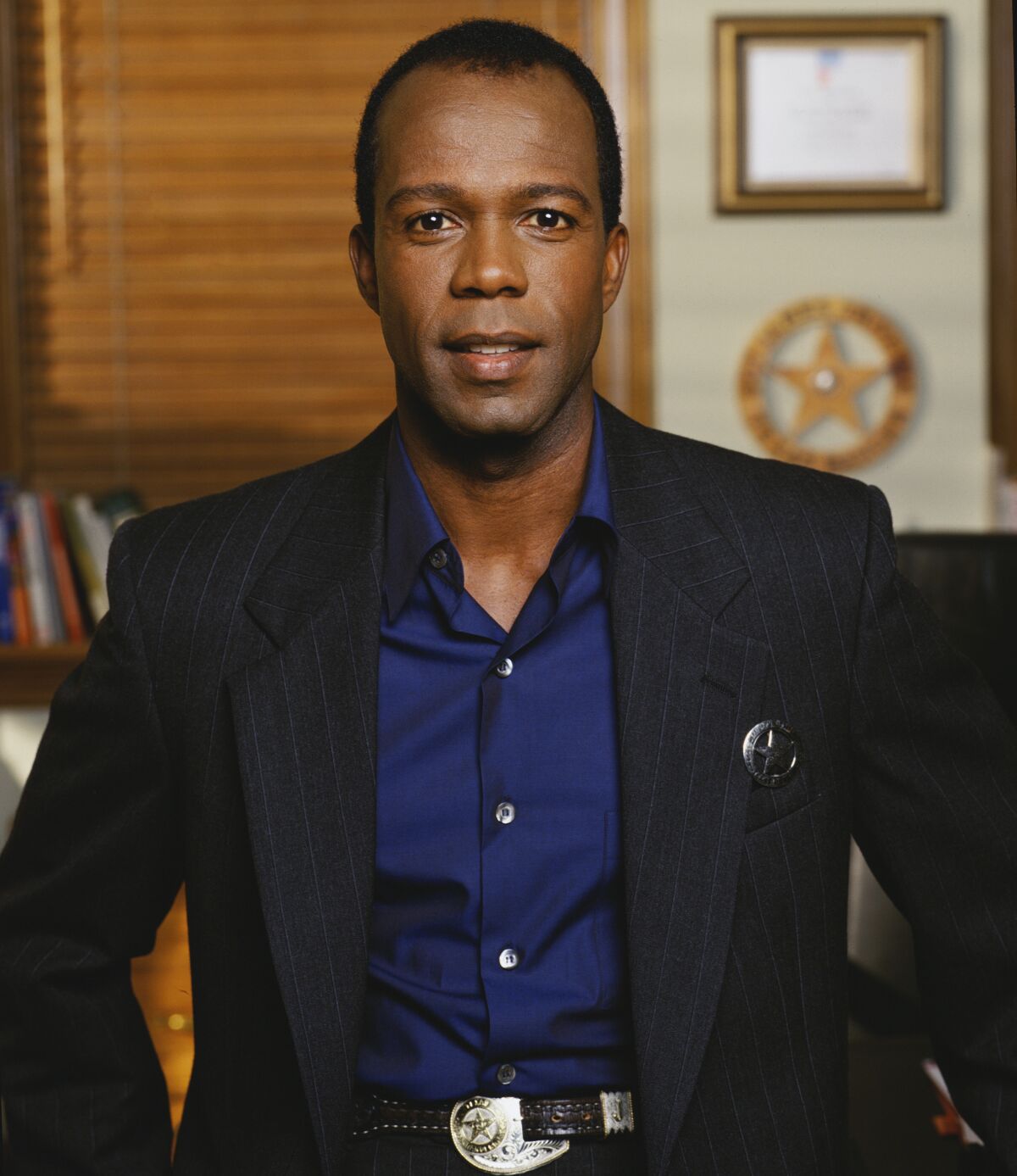 A man with short black hair wearing a black suit and blue collared shirt