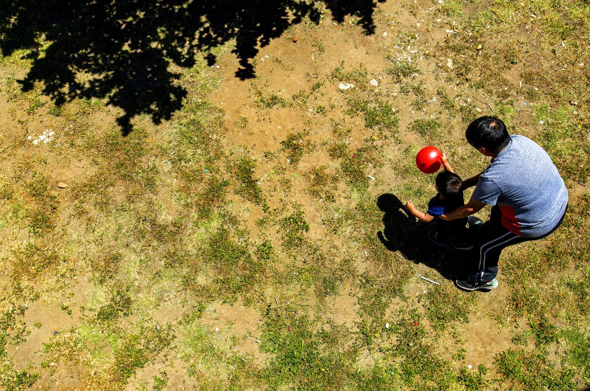 A young child plays with a ball as an adult hovers closeby
