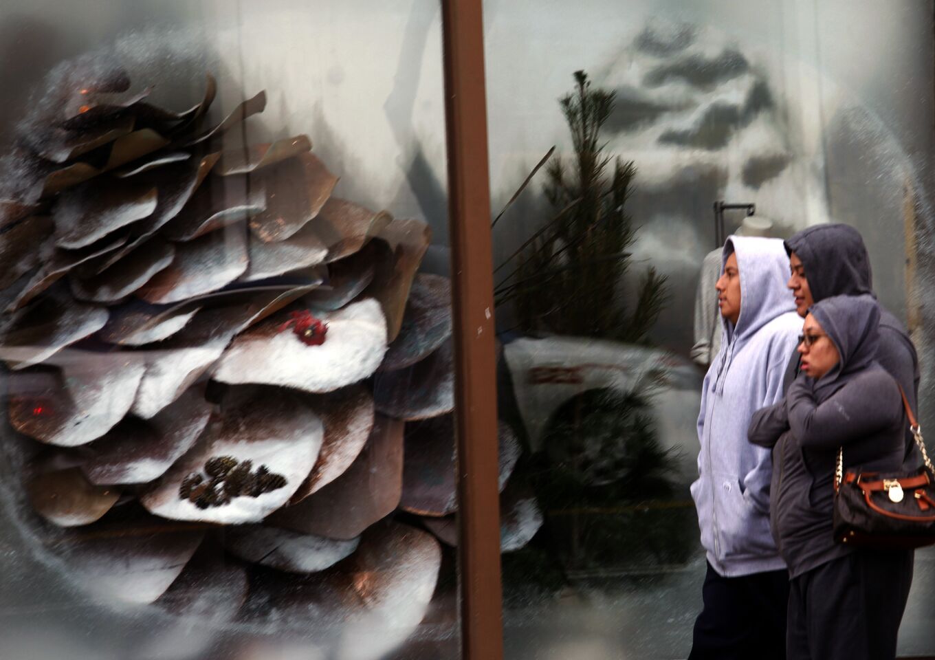Shoppers walk past a winter display on Santa Monica Boulevard in Santa Monica while bracing against the cold and rain Tuesday.