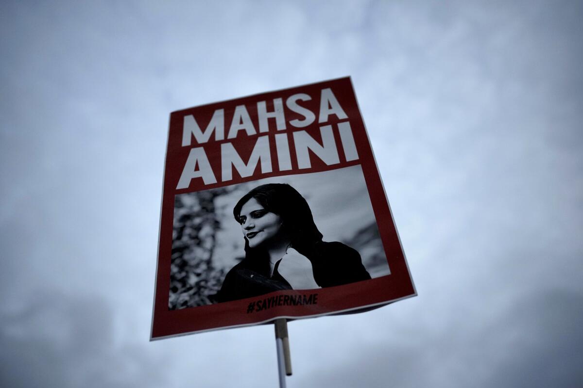 A demonstrator's poster of Mahsa Amini is shown against a cloudy sky