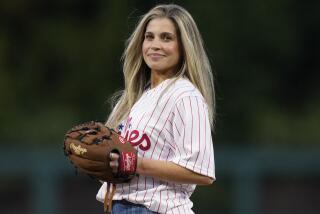 Danielle Fishel wearing a Philadelphia Phillies and baseball glove preparing to throw a ceremonial first pitch before a game