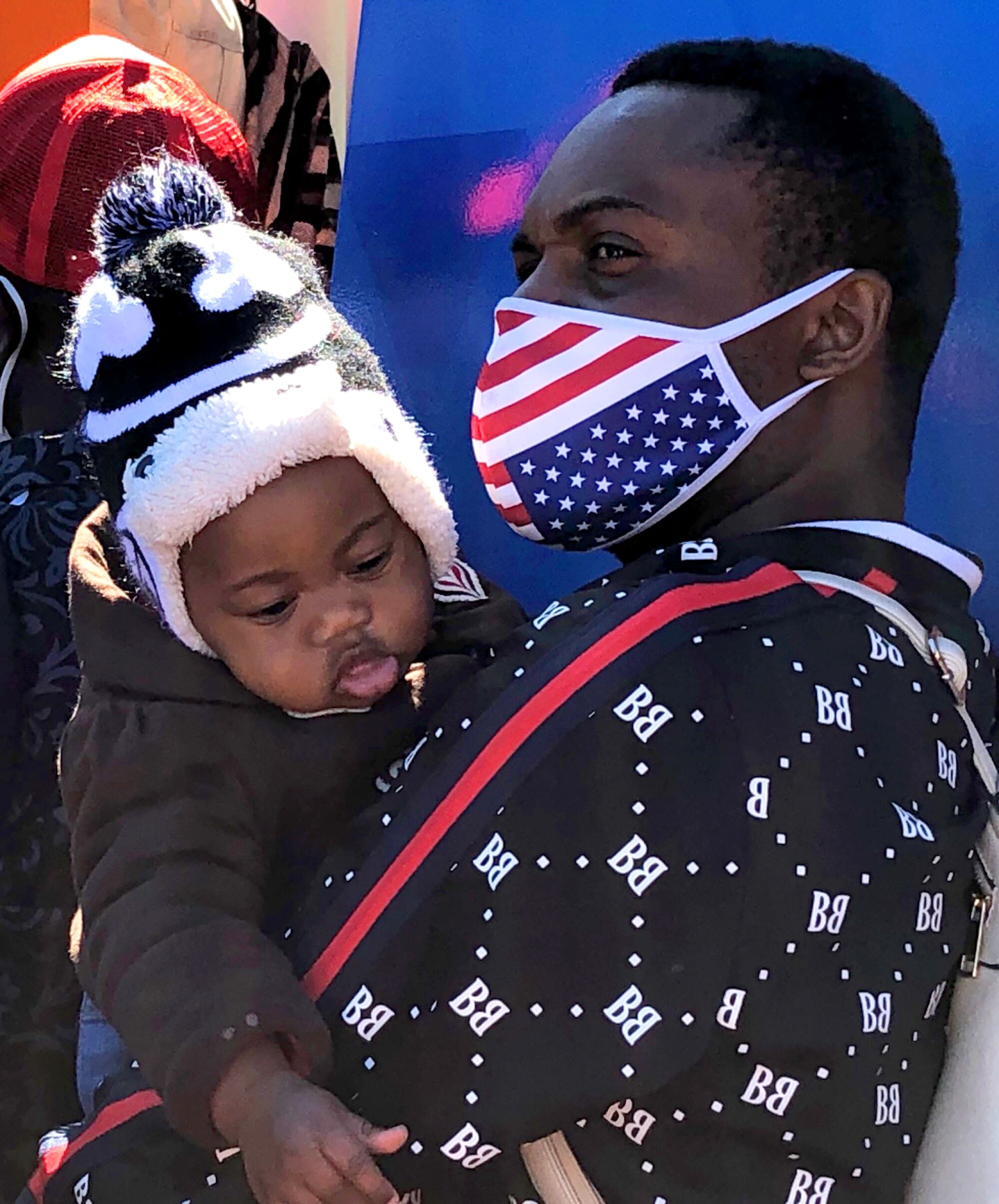 A man in an American flag mask holds his baby. 