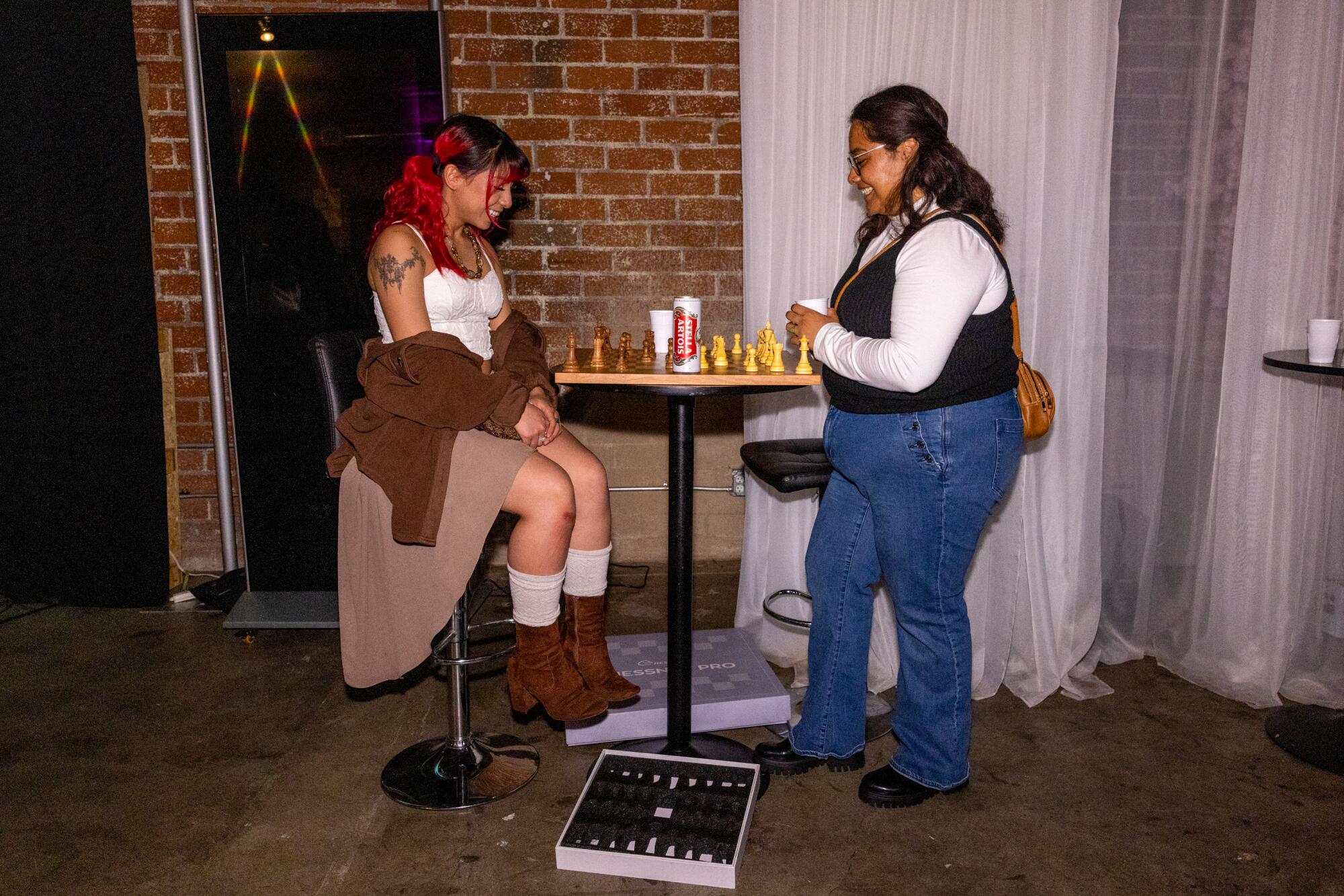 Two friends play a game of chess at a high-top table.