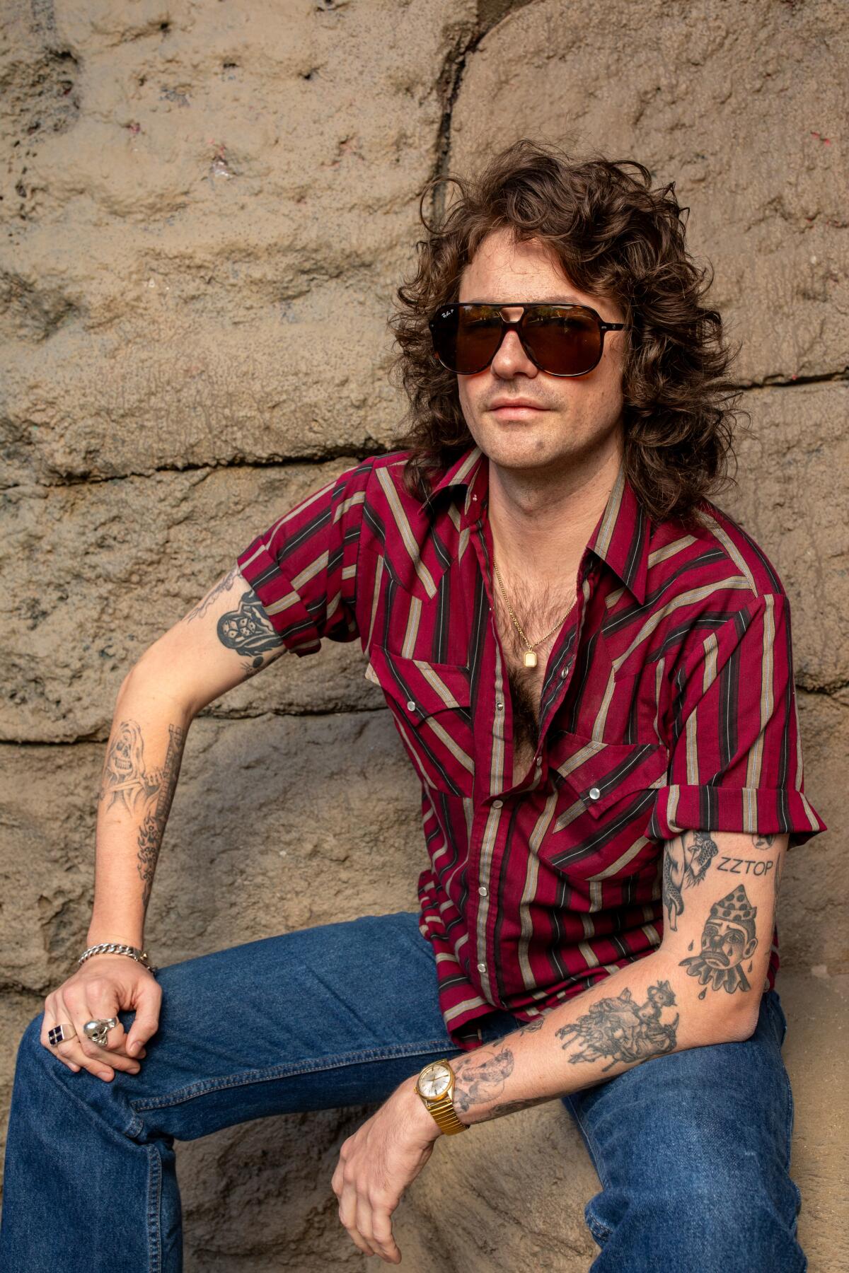 Man with long hair and sunglasses sitting on a rock for a portrait
