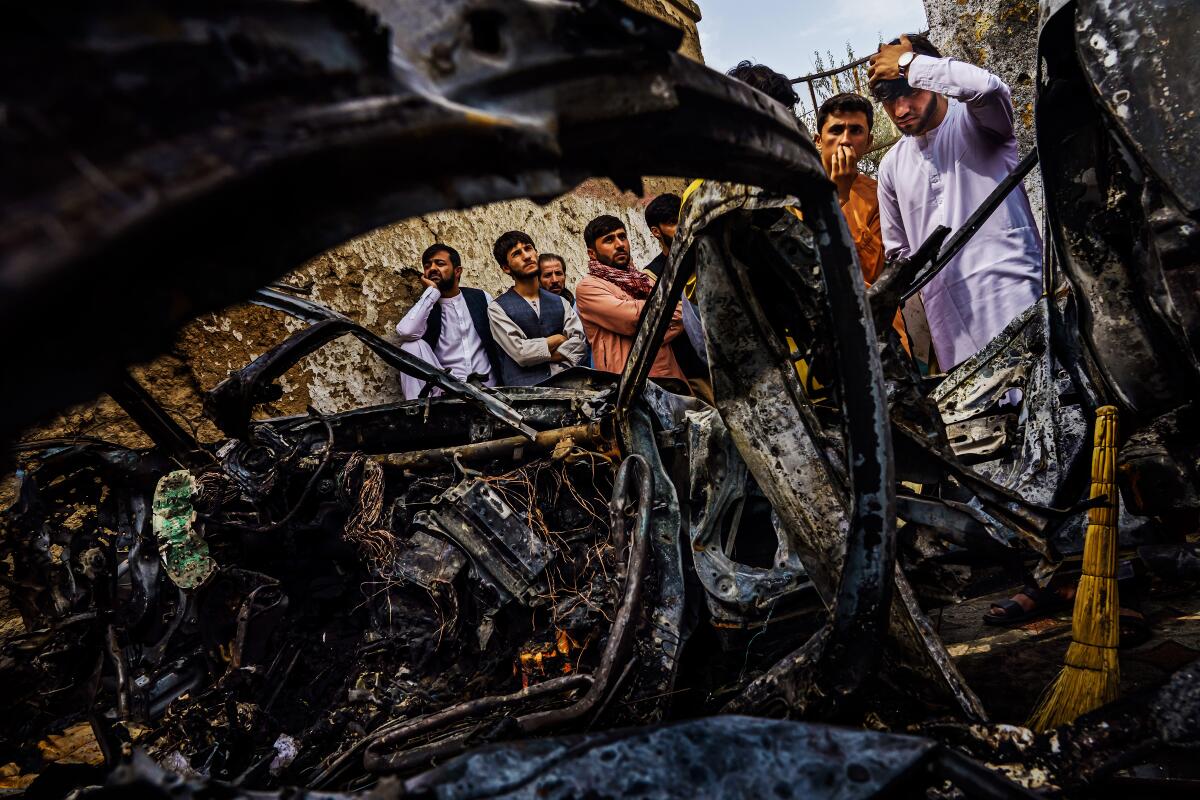 A group of men at the blackened remains of a car.