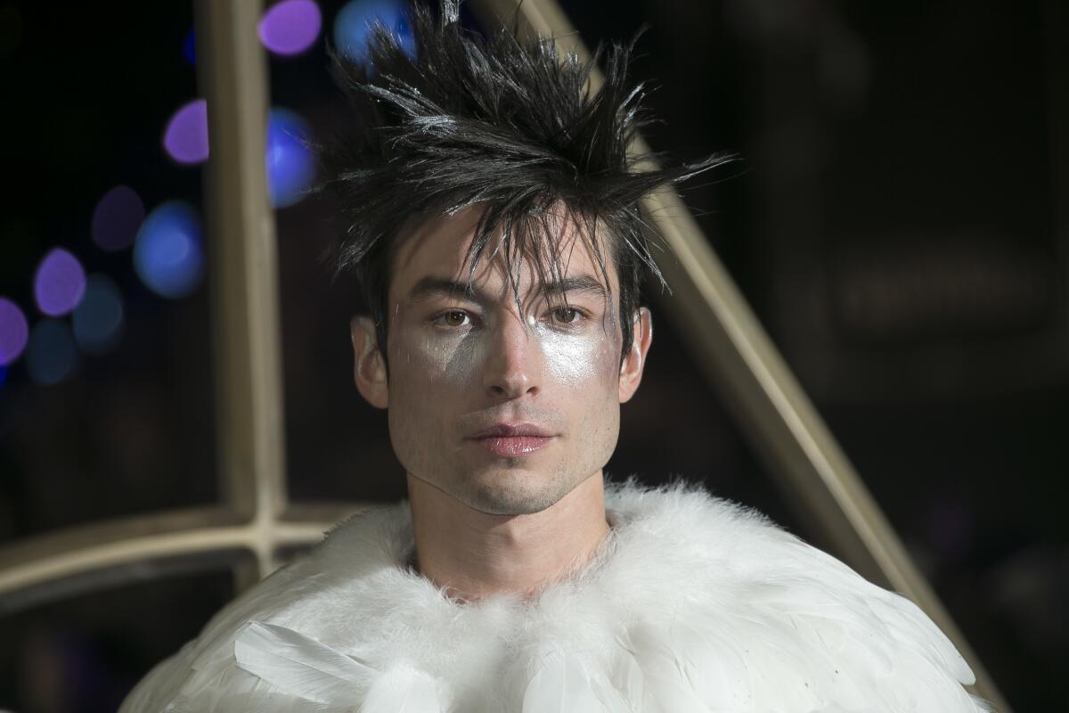 A person with spiky hair and sparkly eye makeup poses for cameras in a feather top