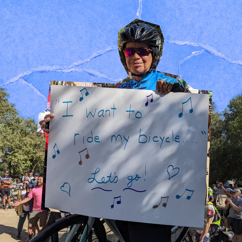 A person in a bike helmet holds a sign that says "I want to ride my bicycle. Let's go!"