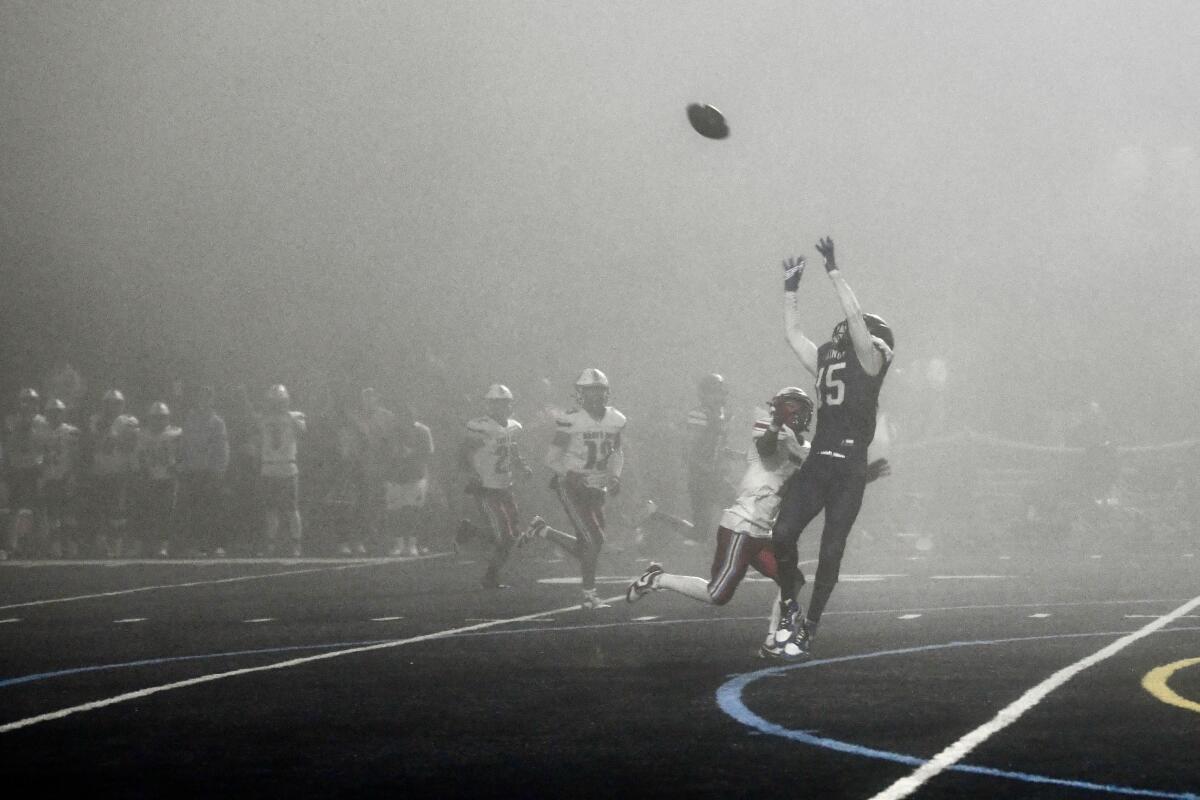 A football player catches a pass on a foggy field.