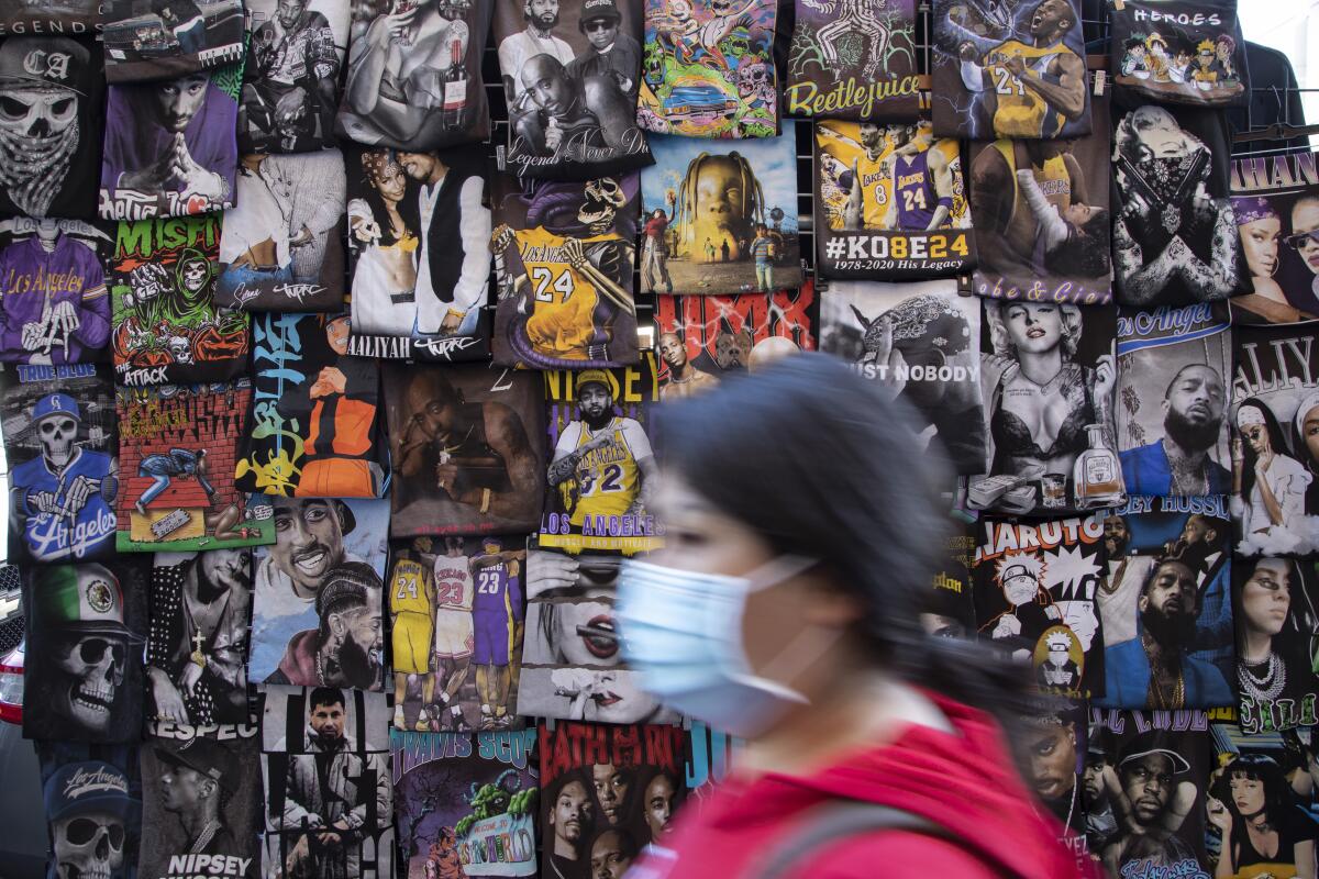 A masked shopper passes a wall of T-shirts in the Fashion District.