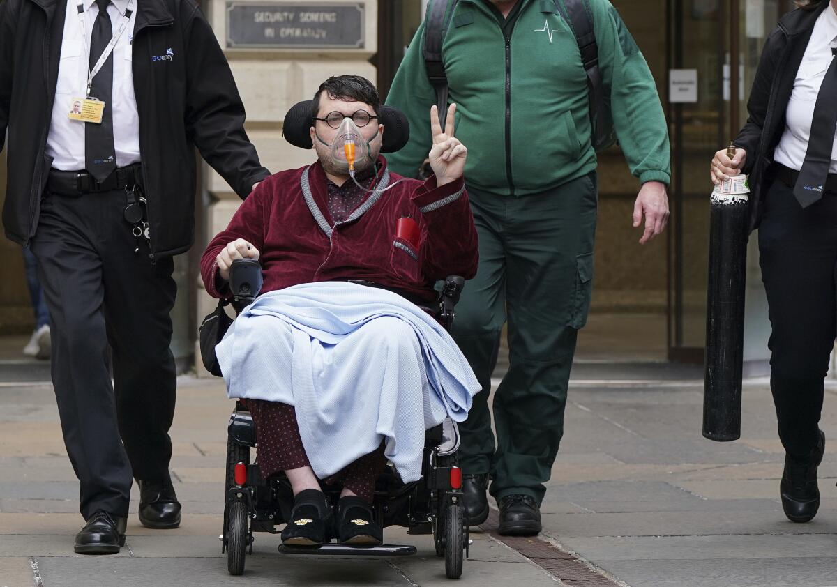 A man in a wheelchair and wearing an oxygen mask flashes a victory sign.