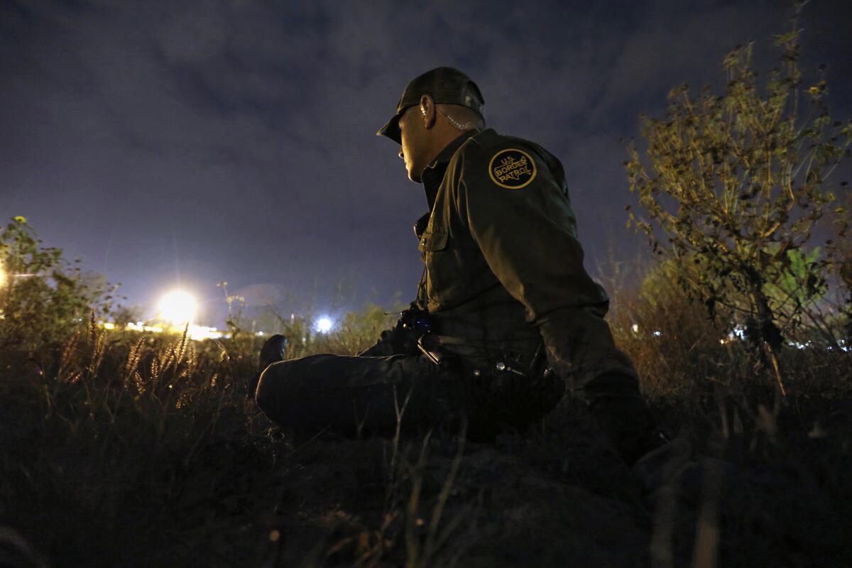 U.S. Border Patrol Agent Robert Trevino stays low as he waits for migrants to cross the Rio Grande in Roma, Texas.