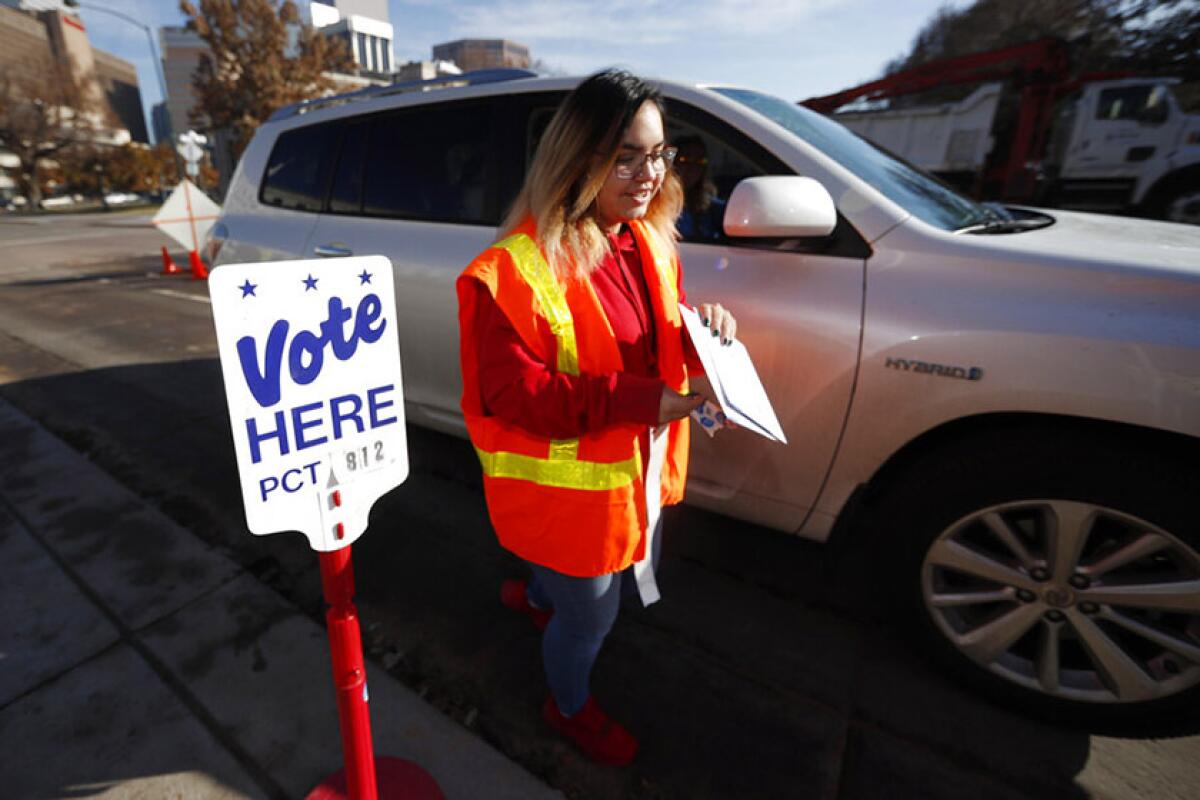 Election judge Amanda Vigil collects a ballot Nov. 5 at a drive-through site in Denver.   