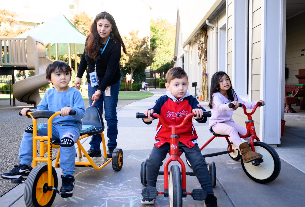 A teacher with three toddlers on tricycles