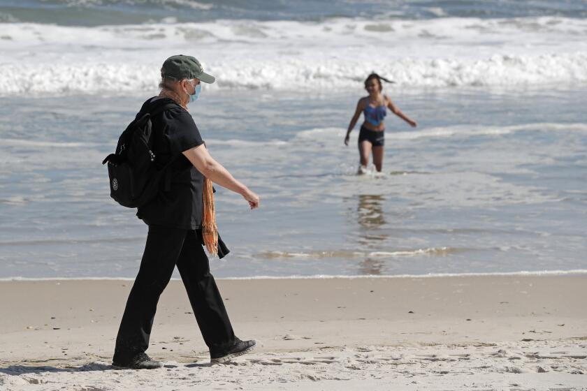 A woman wears a protective face mask during the current coronavirus outbreak, Thursday, May 21, 2020, as she walks on Jones Beach in Wantagh, New York. As pandemic lockdowns ease across the United States, millions of Americans are set to take tentative steps outdoors to celebrate Memorial Day, the traditional start of summer. But public health officials are concerned that if people congregate in crowds or engage in other risky behaviors, the long weekend could cause the coronavirus to come roaring back. (AP Photo/Kathy Willens)