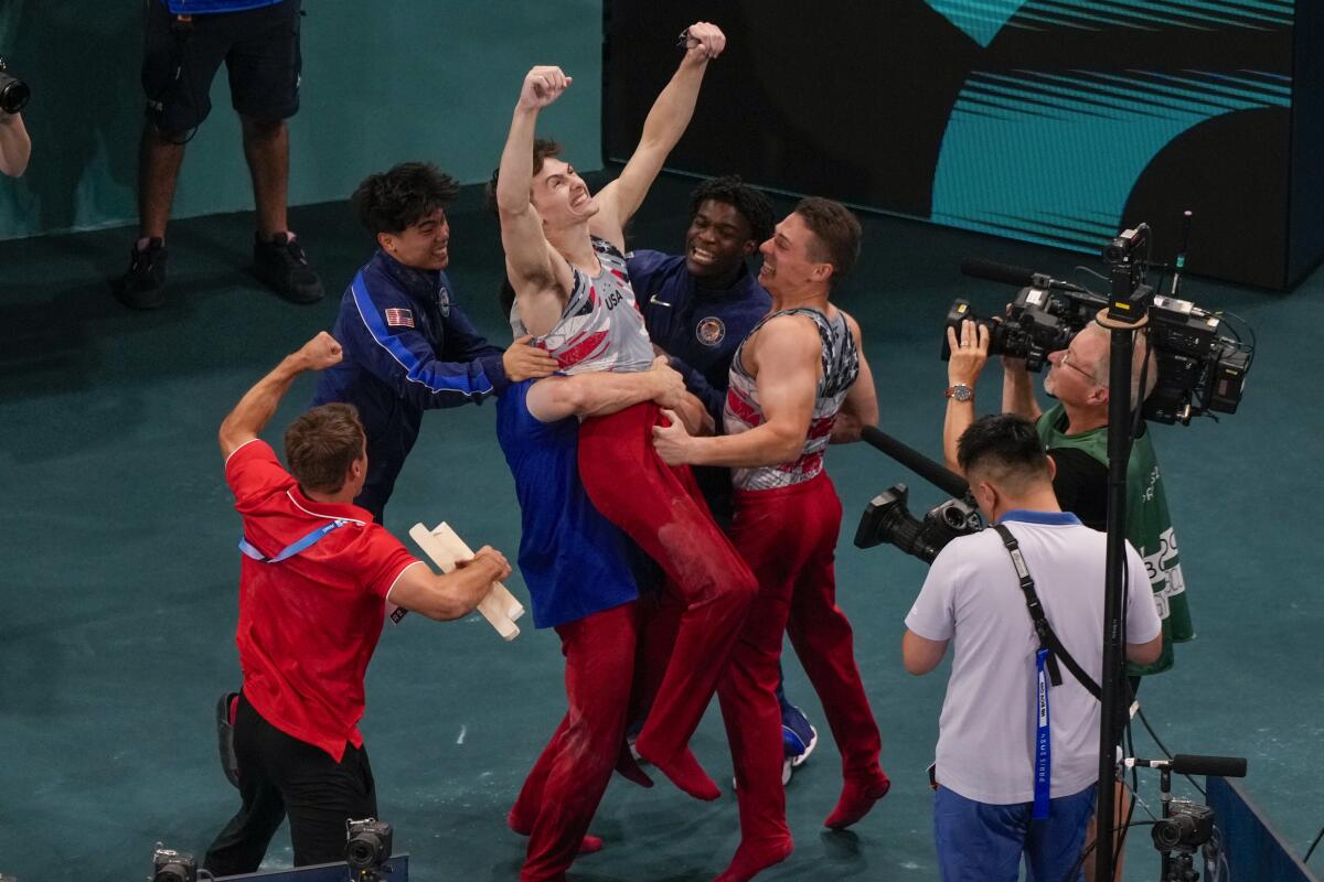 American Stephen Nedoroscik raises his arms while being picked up from behind and congratulated by team members.
