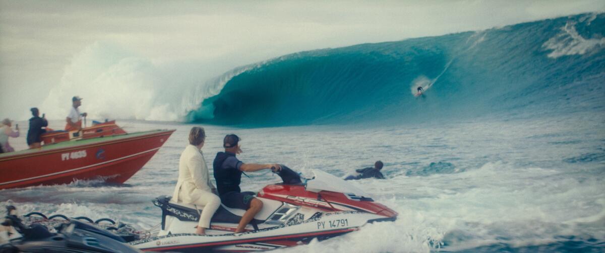 A surfer rides a giant wave while others on a boat and jet ski watch.
